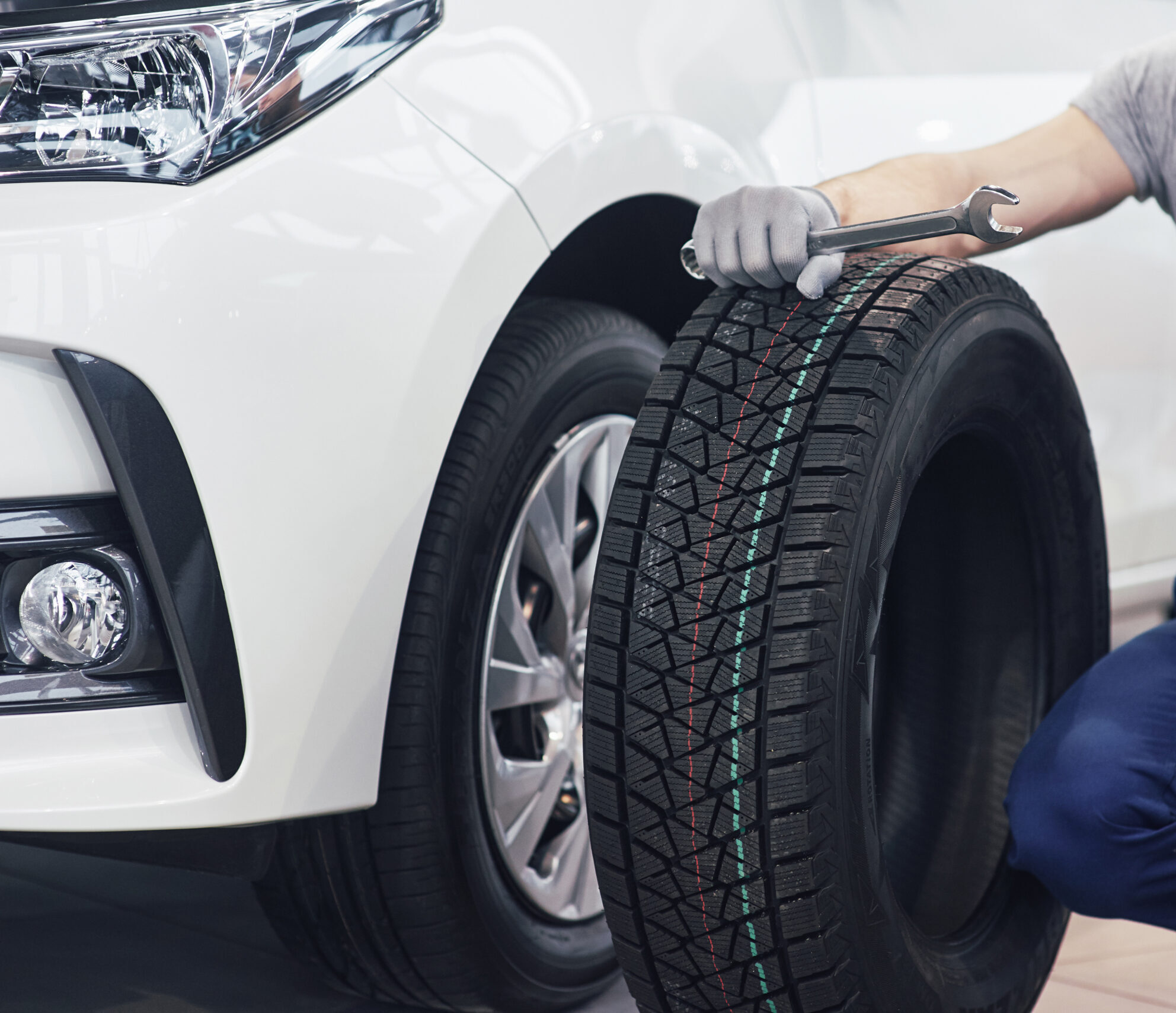 Technician with a blue workwear, holding a wrench and a tire while showing thumb up Technician with a blue workwear, holding a wrench and a tire while showing thumb up